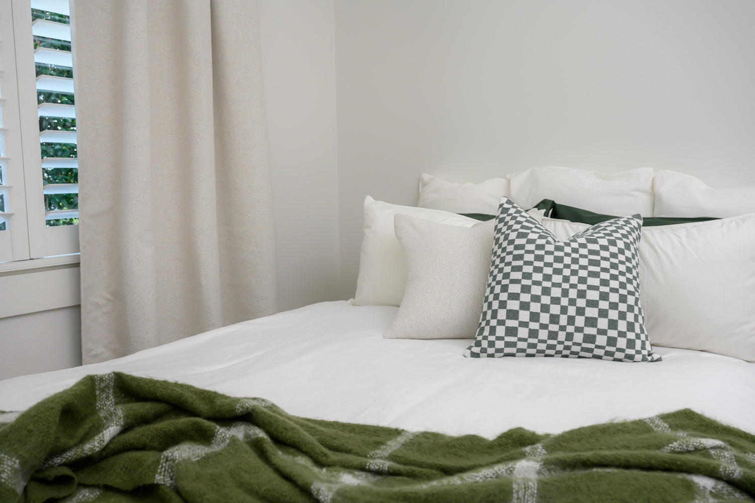 Brooklyn Boucle curtain styled in a bedroom with sage accents, featuring Chicago Check cushion in Sage and Brooklyn Boucle cushions for a cool, modern look.