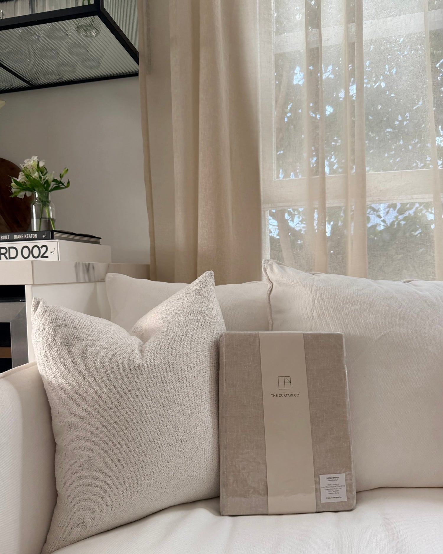 The Soho Linen Blend Sheer in Natural packaging styled on a couch.